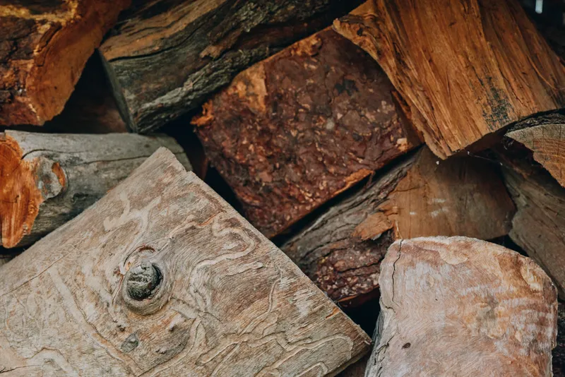 Firewood, logs, woodpile, stacked wood, cut wood, timber. Close-up of rustic firewood pile outdoors with rough bark texture, seasoned hardwood for winter fireplace, cozy cabin heating fuel.