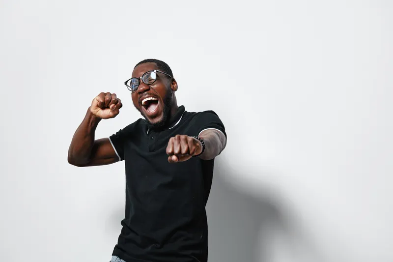 African American man with dark skin wearing glasses and black shirt, smiling and dancing with energetic gesture on white background for happiness and lifestyle concept.