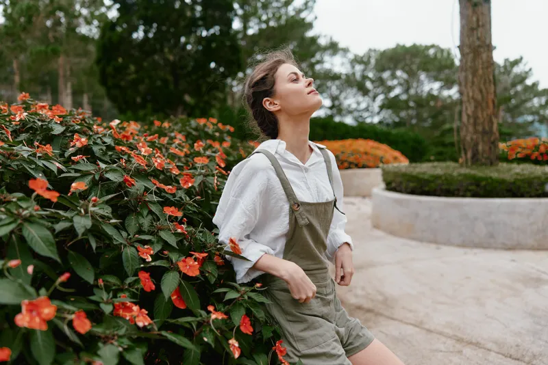 Young woman enjoying nature in a garden full of vibrant flowers, wearing a stylish outfit, radiating joy and relaxation on a sunny day