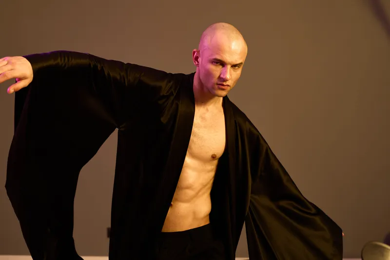 Stylish man in black and white attire poses dramatically against a muted background, showcasing confidence and artistic flair. Unique fashion choice adds visual intrigue.