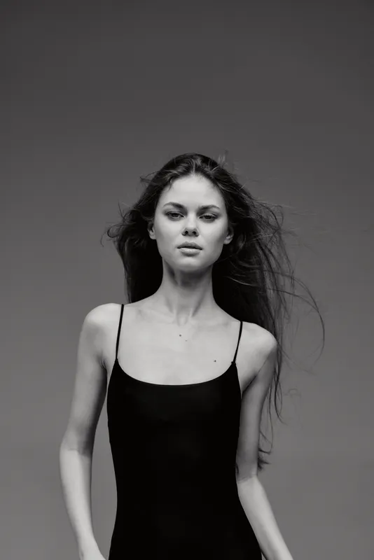 Black and white portrait of a serious young woman with long hair wearing a black dress against dark background