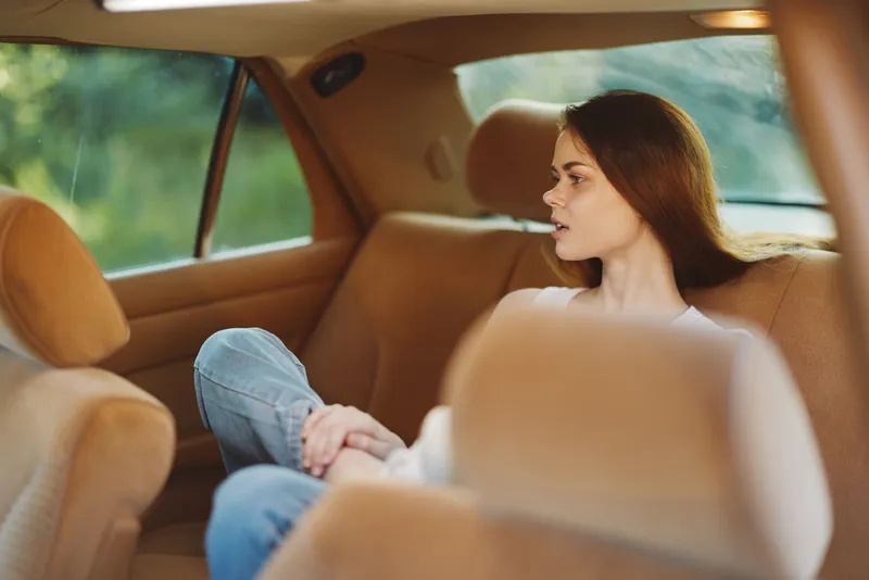 Young woman relaxing in a car, dressed casually in jeans and a white top, with a serene expression and nature in the background, perfect for lifestyle themes.