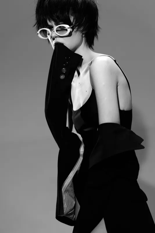 Black and white portrait of a stylish woman wearing glasses and a blazer with short hair and a pensive mood