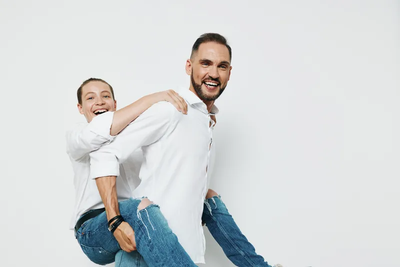 A confident business professional man carries a joyful colleague on his back against a bright white background, radiating teamwork, energy, motivation, and strong positive emotion.