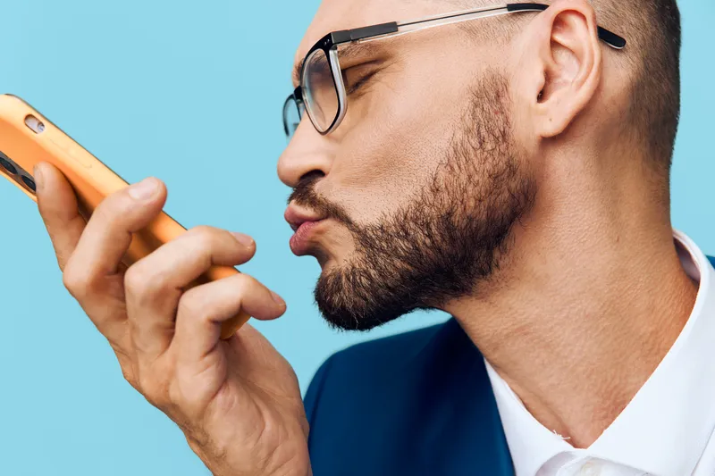 Professional man in business attire on a colored isolated background, displaying focused emotion as he speaks into a smartphone with confidence and purpose.