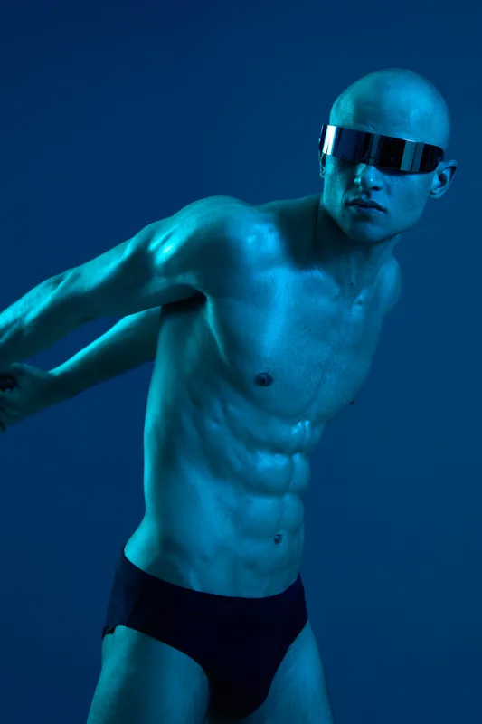 Athletic man posing confidently, wearing sunglasses and swimwear, showcasing a fit physique. The composition is vibrant, emphasizing bold colors.