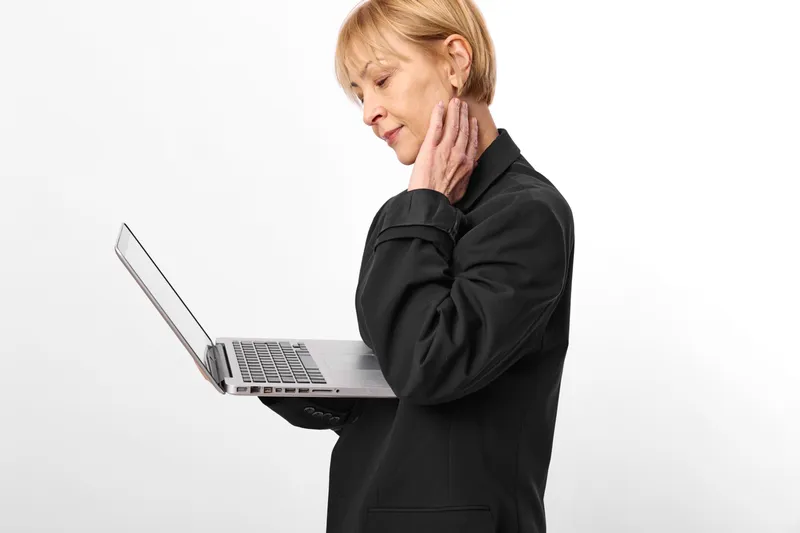 Senior woman with laptop in studio, business outfit, hand on ear, headache, phone communication, modern technology, white background, soft light, female