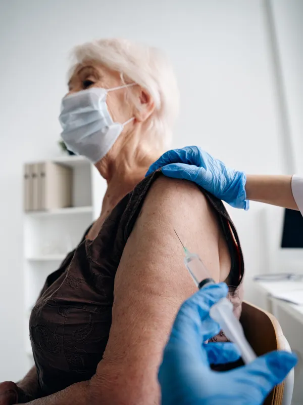 Врач делает пожилой женщине инъекцию вакцины от COVID-19