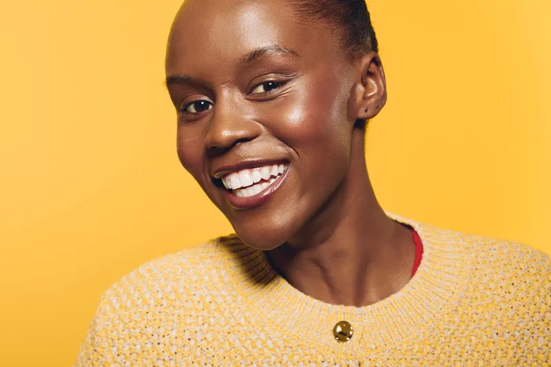 Smiling African woman with dark skin wearing a yellow sweater on yellow background. Close-up portrait of happy black female model with natural beauty and positive expression.