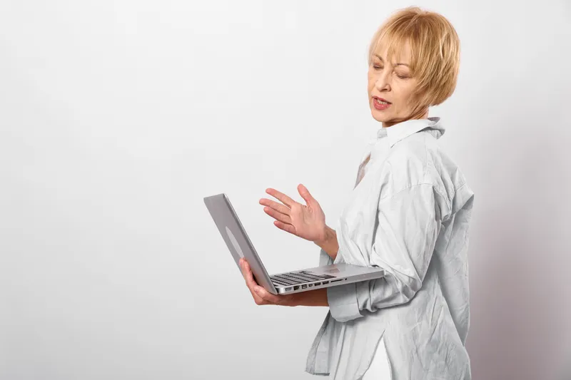 An anxious woman with short hair gestures while using a laptop, indoor studio background, focused communication for remote work, concept for stress and mental health