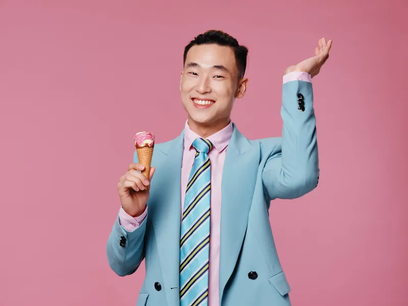 Мужчина азиатской внешности в синем костюме держит в руках мороженое, на розовом фоне