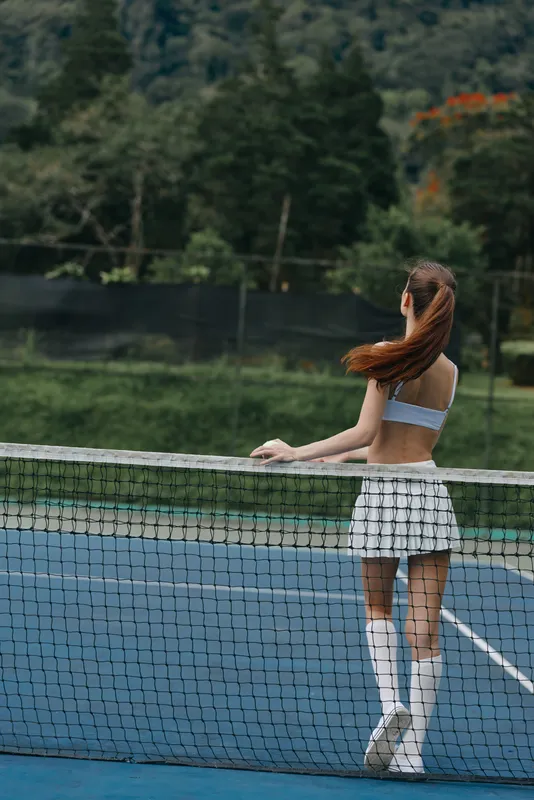 Young athletic woman in sportswear enjoying a moment on the tennis court, showcasing a serene expression and vibrant surroundings in lush greens