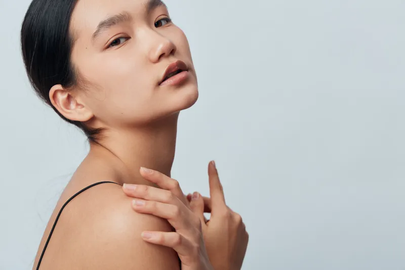 Portrait of young woman with natural skin closeup, bare shoulders and smooth complexion against light background. Beauty, skincare and healthy face with calm expression and minimal makeup.