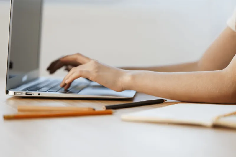 Close up of a young female s hands typing on a laptop, showcasing a modern workspace, with a focus on productivity and creativity in a bright, neutral colored environment