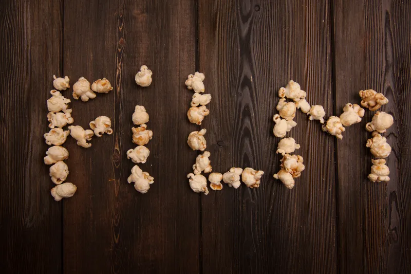 На деревянном фоне выложено слово «MOVIE» из попкорна