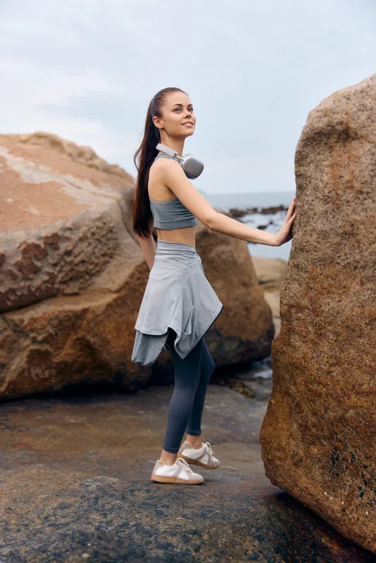 Young athletic woman in sporty outfit stands on rocky coastline, showcasing active lifestyle and healthy living amidst natural scenery