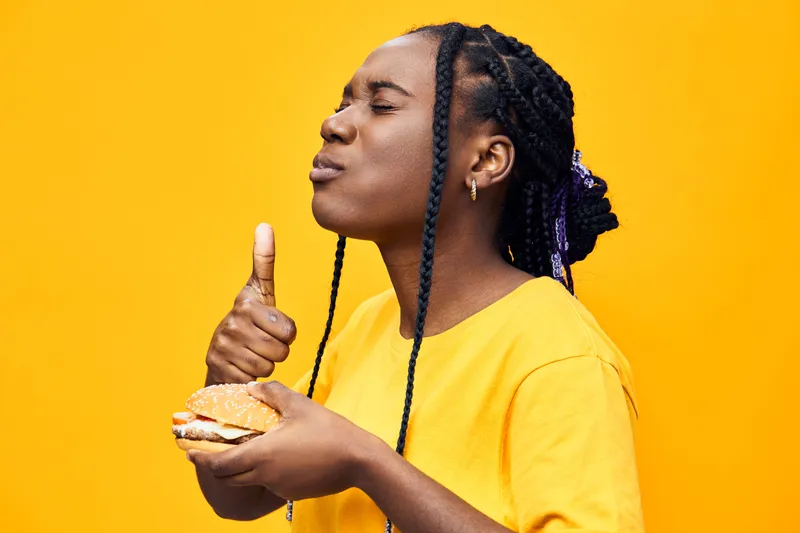 African woman enjoying a delicious sandwich, showing pleasure and satisfaction against a bright yellow background Perfect for healthy eating concepts