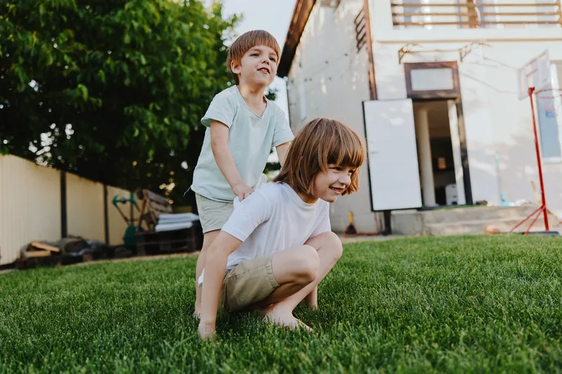 Two playful boys enjoying a sunny day in the backyard, one riding on the back of another, creating a joyful atmosphere of childhood fun and laughter.