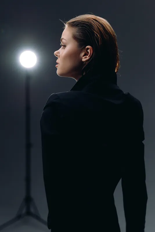 Profile of a thoughtful woman in dark clothing against blurred studio light, showcasing sophistication and calm expression.