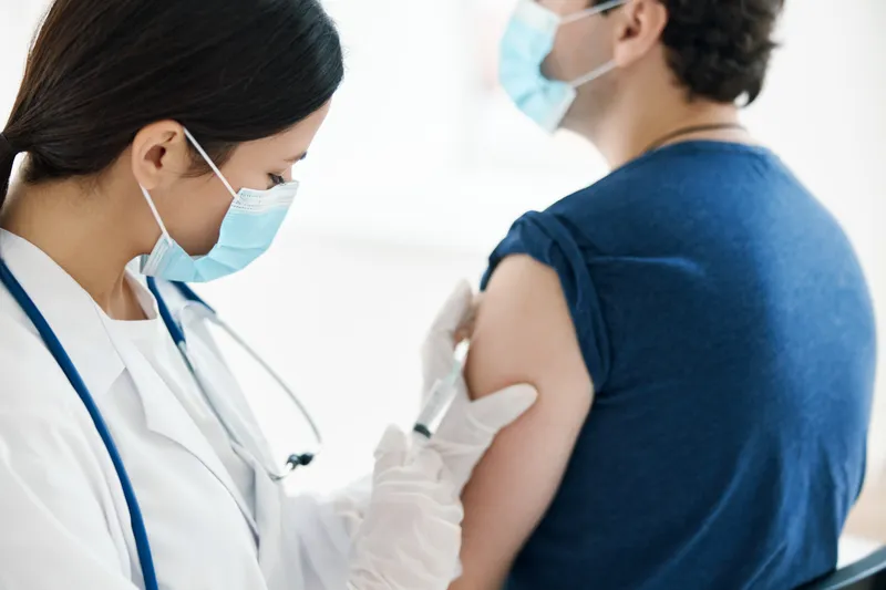Медсестра в медицинской маске делает инъекцию вакцины в плечо пациента