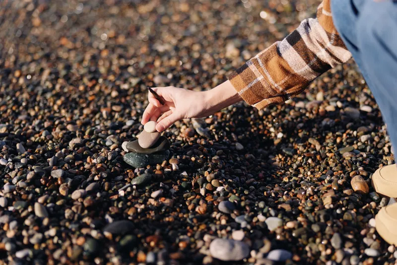 Hand on pebbles at the beach, closeup of stones and sandy texture, capturing outdoor activity, careful handling, and simple exploration of the shoreline in natural light and breeze.
