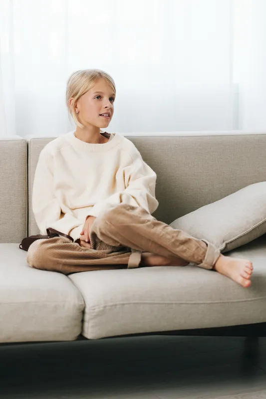 Authentic lifestyle scene introducing a young student at home, relaxing on a sofa, embracing simple play and study moments in a cozy, calm setting.