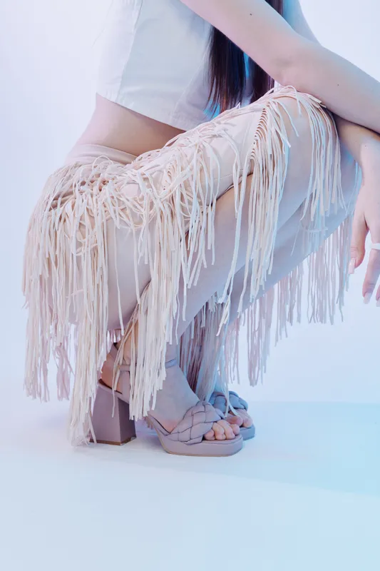 Woman beauty fashion concept with a close-up of a female model wearing fringed pants and high heel sandals. Studio shot with soft lighting emphasizing style and elegance.
