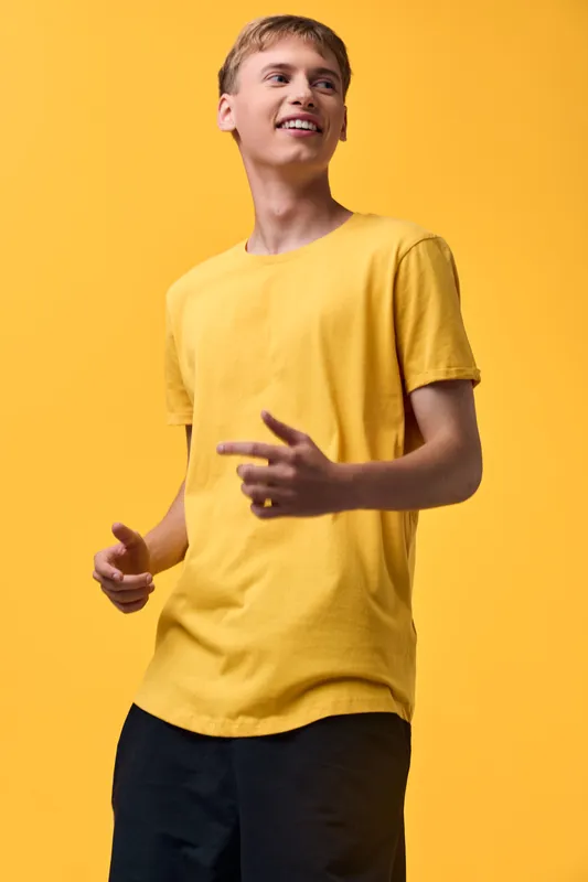 Yellow shirt, casual fashion, upbeat pose, smiling man, bright background, urban style, contemporary wardrobe, relaxed confidence, vibrant tones, energetic and approachable imagery