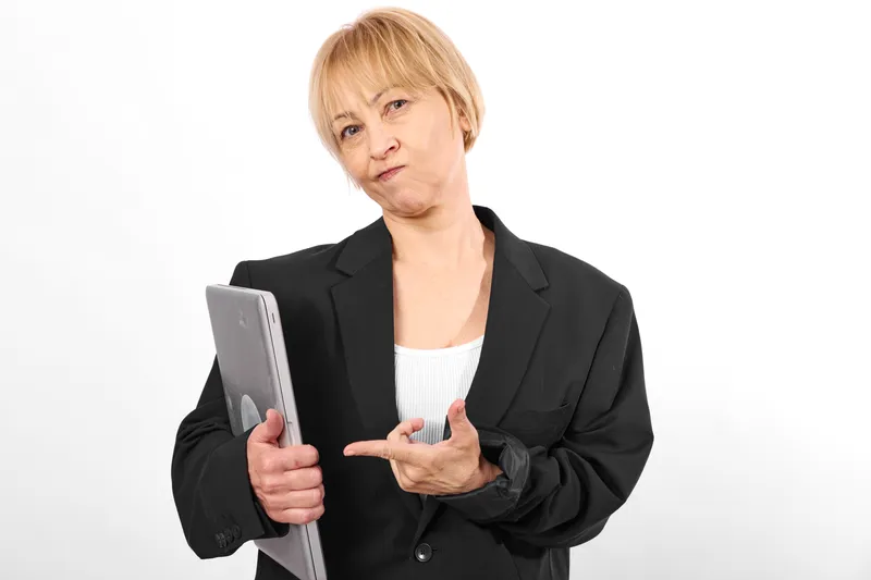 Woman in business blazer holding tablet, shushing gesture, focused expression, studio portrait on white background, soft even light, modern communication concept for support