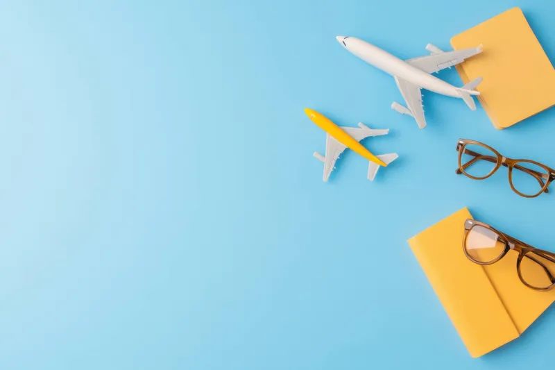Планирование отпуска в стиле flat lay: модели самолетов, дорожные журналы и очки на безмятежном голубом фоне