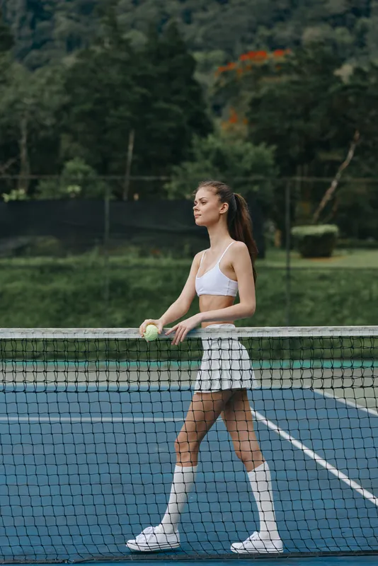 Young athletic woman playing tennis on a sunny day, wearing a white sports outfit, radiating confidence and joy while holding a tennis ball on a court