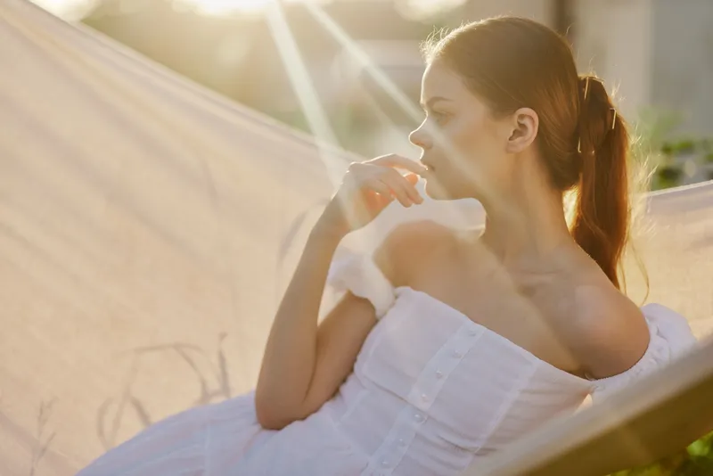 Serene young woman in a white dress relaxing outdoors, capturing tranquility and sunlight during a peaceful moment in nature