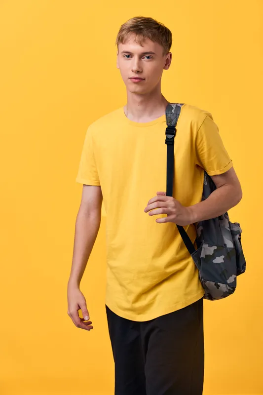 Student youth wearing casual clothing with a backpack against a bright yellow backdrop, showcasing everyday style, mobility and confidence for fashion, education and youth culture themes