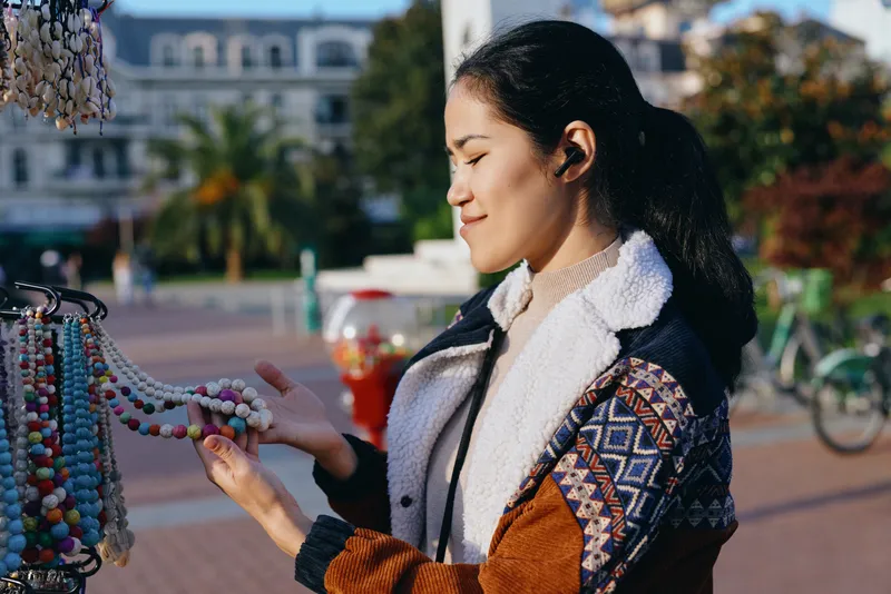 Beads, jewelry, market mood capture an outdoor scene as a woman admires colorful accessories and handmade craft, casual jacket in sunlight, vibrant textures, artisan vibe and street style
