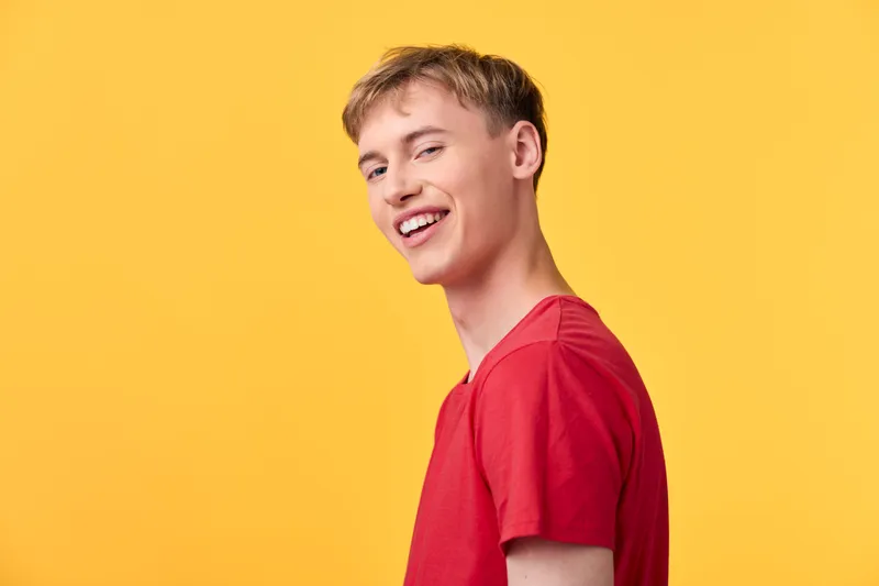 Smiling young man in a red t shirt against a vibrant yellow background, casual studio setting, cheerful expression and friendly energy, suitable for lifestyle, fashion, youth and positivity themes