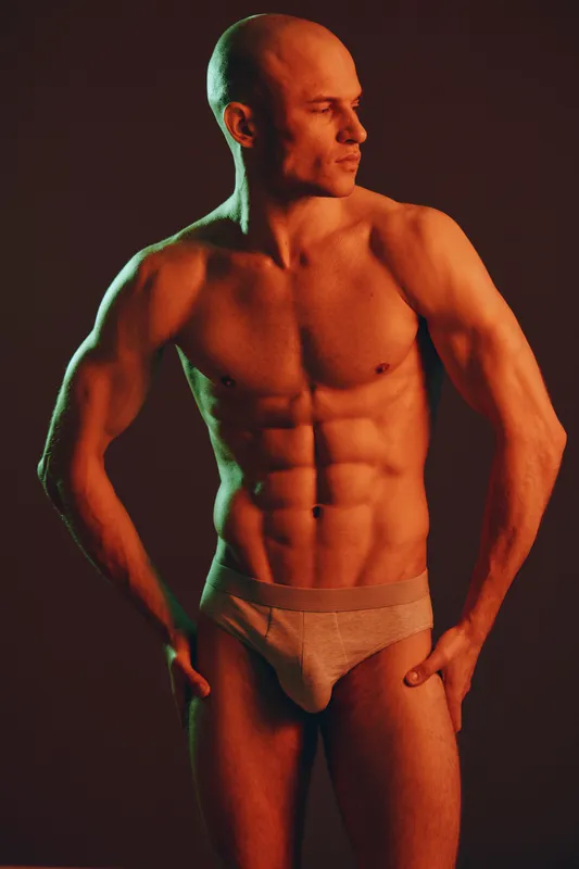 Muscular man posing confidently in low light, showcasing strong physique and defined abs against a dramatic background. Black and white art photography concept.