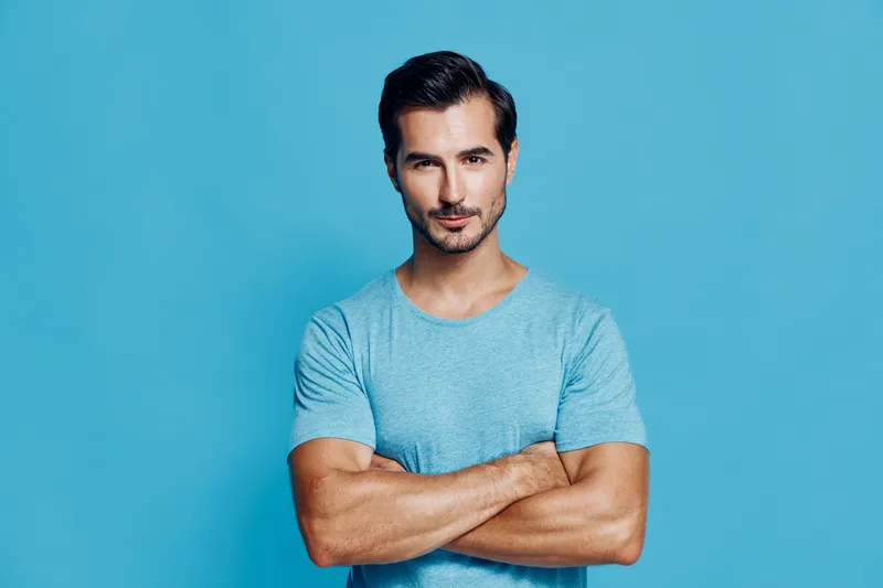 Confident man in blue t-shirt standing with folded arms on solid bright blue background. Portrait showcasing strong features and relaxed attitude, studio shot.