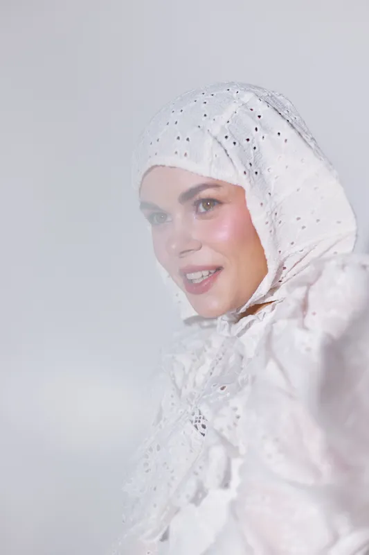 Young woman in a white hijab, smiling softly against a light background, embodying modern modest fashion with a fresh and ethereal vibe
