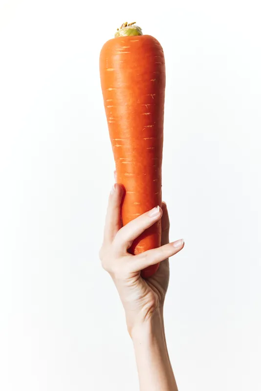 Рука держит свежую морковь, а в углу изображения расположено слово «carrot»