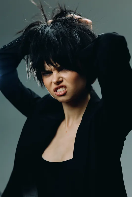 frustrated woman with black hair pulling hair wearing dark clothes in moody lighting
