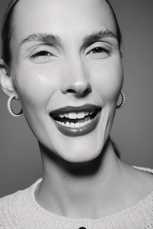 Close-up portrait of a smiling white woman with light skin and hoop earrings, expressing joy and happiness in studio lighting.