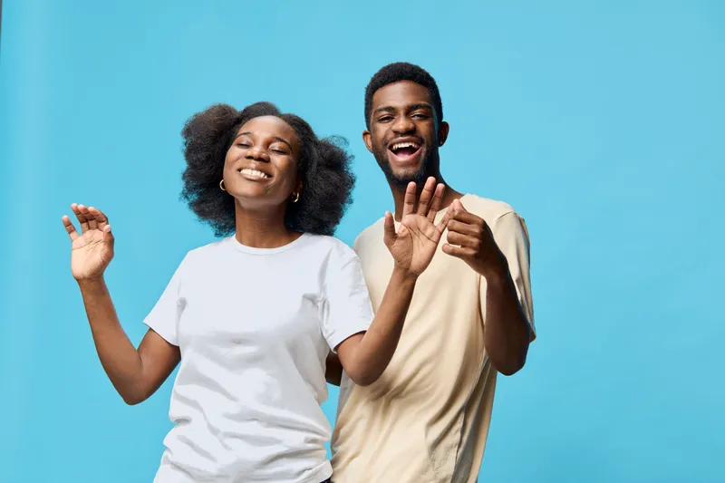 Young joyful couple dancing together against a vibrant blue background, expressing happiness and connection with natural hairstyles and casual clothing