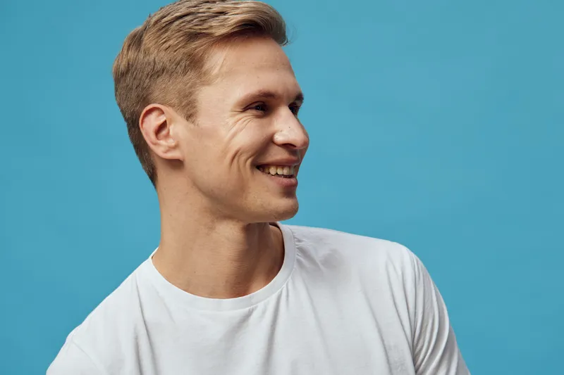 Smiling happy young caucasian man in white t-shirt looking aside with joyful expression blue background casual lifestyle concept