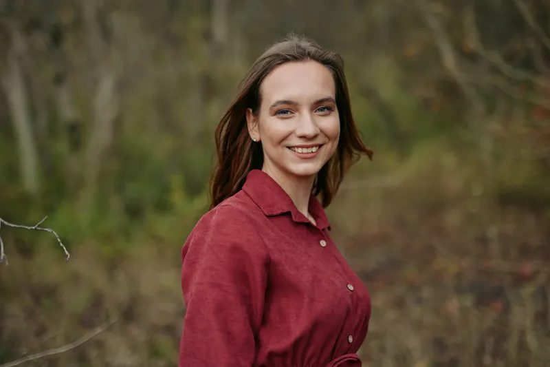 Natural outdoor portrait of a smiling young woman in a red dress, conveying relaxed confidence and genuine connection; emphasis on authenticity and credibility in candid expression.