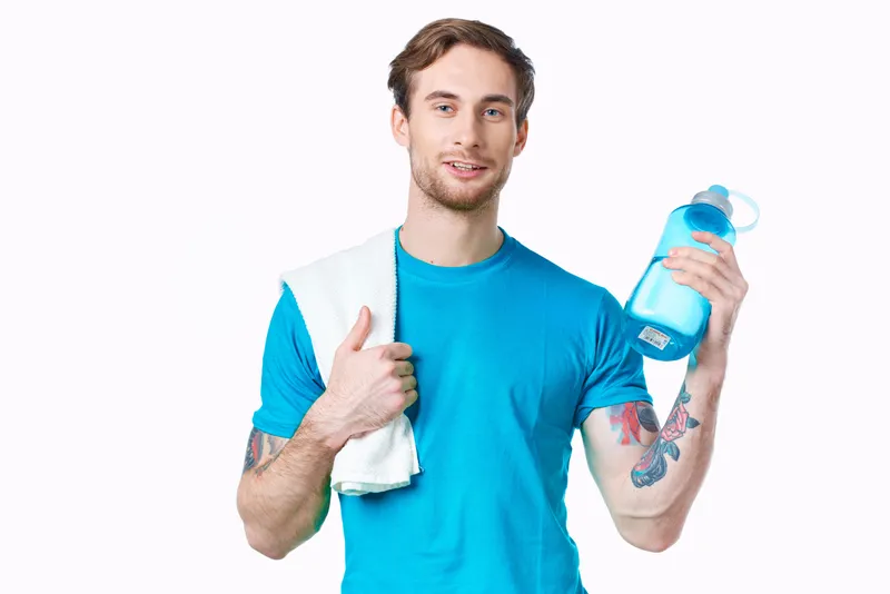 Мужчина в синей футболке с бутылкой воды, занимающийся фитнесом