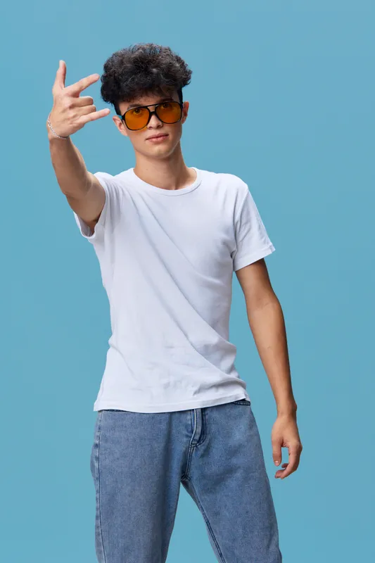 Young man wearing sunglasses and casual clothes showing a hand gesture against a solid blue background, expressing cool and relaxed attitude.