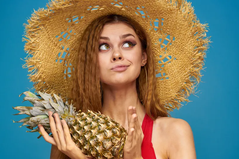 Женщина в соломенной шляпе с ананасом в руках, или это веселье, синий фон, экзотические фрукты