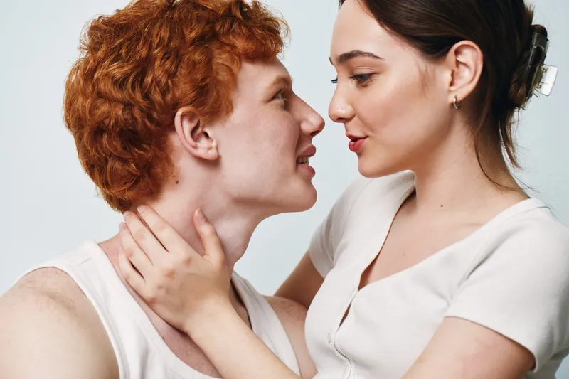 Couple, young man and woman looking at each other with affection and intimacy. Redhead male and brunette female in casual clothes sharing close moment of love and connection indoors.