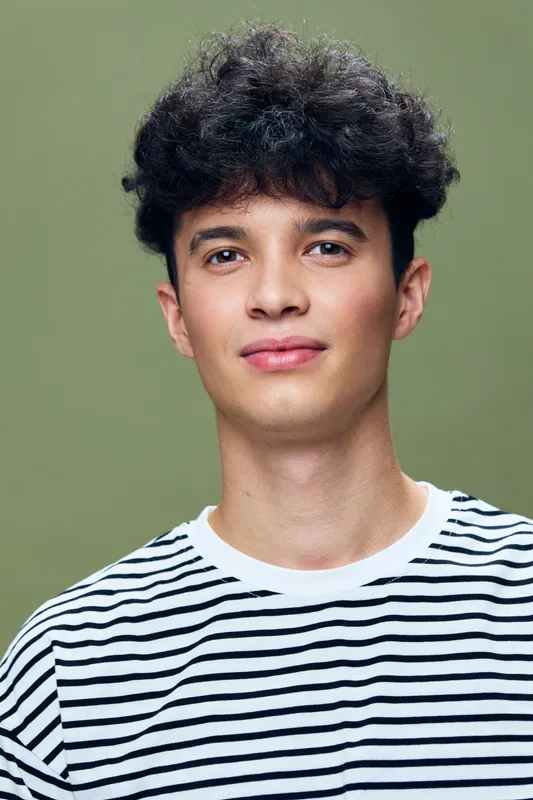 young man wearing black and white striped shirt standing against green background with calm expression and natural curly hair, casual portrait with soft lighting