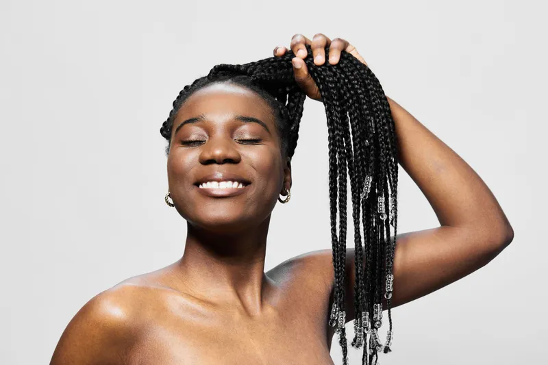 Joyful African woman with braided hair smiling, showcasing elegance and beauty, perfect for hair care and beauty concepts, against a simple gray background